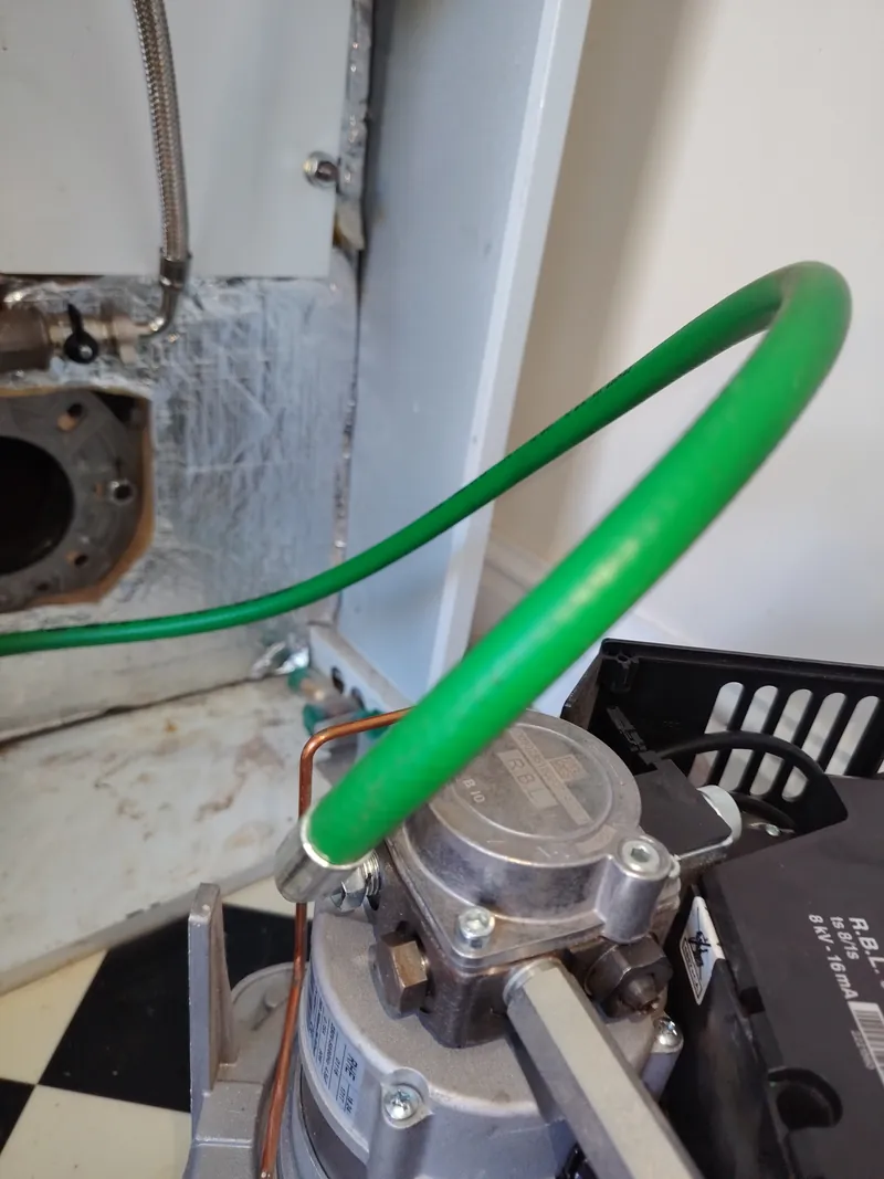 Riello burner removed from a Grant Vortex Pro oil boiler with the green oil supply hose disconnected, showing the empty combustion chamber opening
