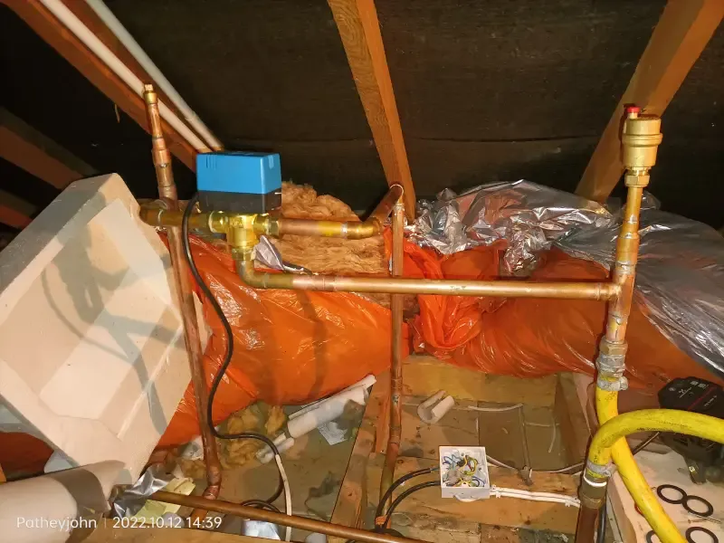Central heating pipework and motorised zone valve in a loft, part of a heating system being flushed in Exeter